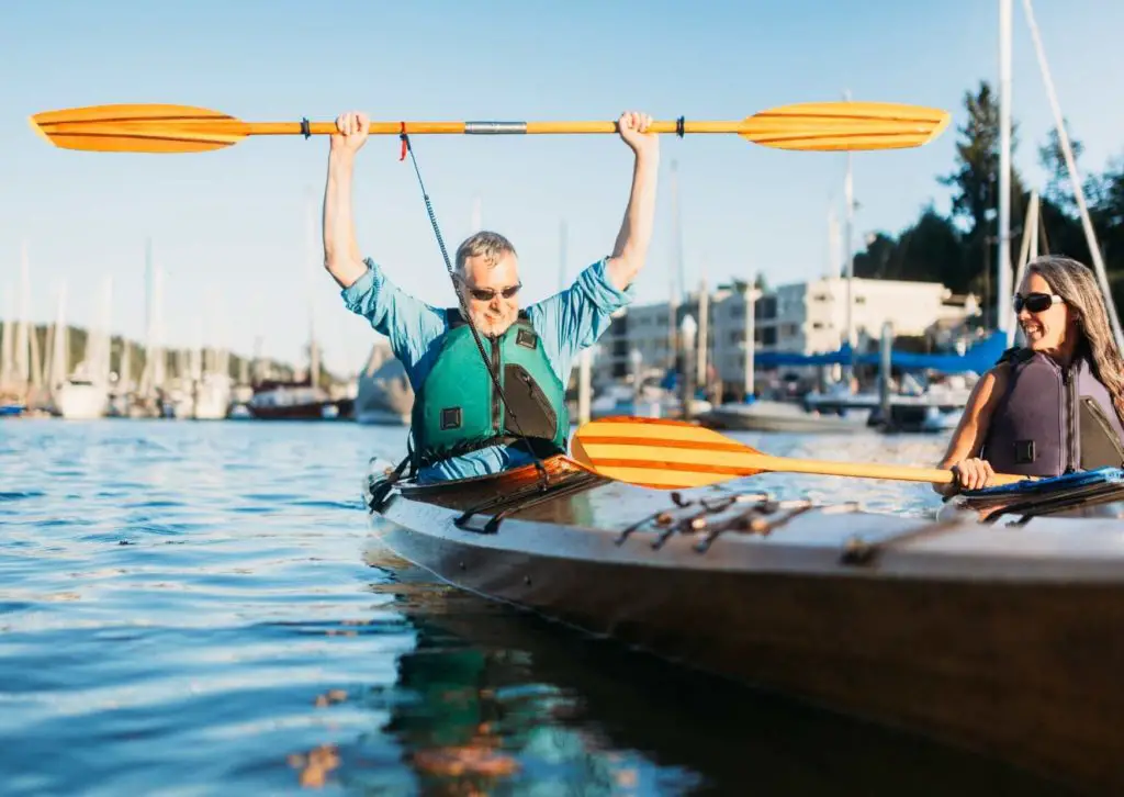 A man in a kayak holding up a paddle asking why should you get a kayak